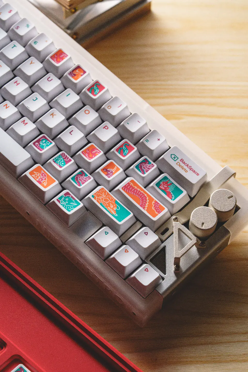 Right side of a white keyboard with colorful creature keycaps beside two control knobs.