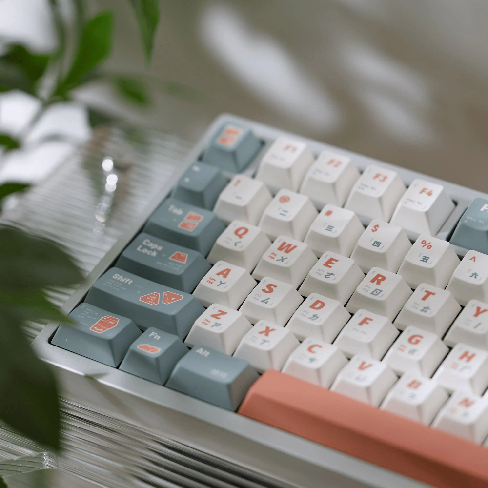 Close view of gray-green, white, and salmon GUARDIAN keycaps with leaves in the foreground.