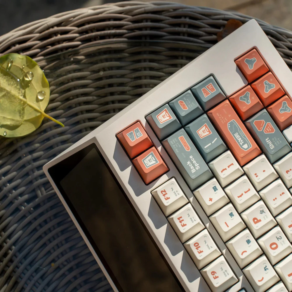 Angled close-up of the upper corner of a keyboard using GUARDIAN keycaps beside a leaf.