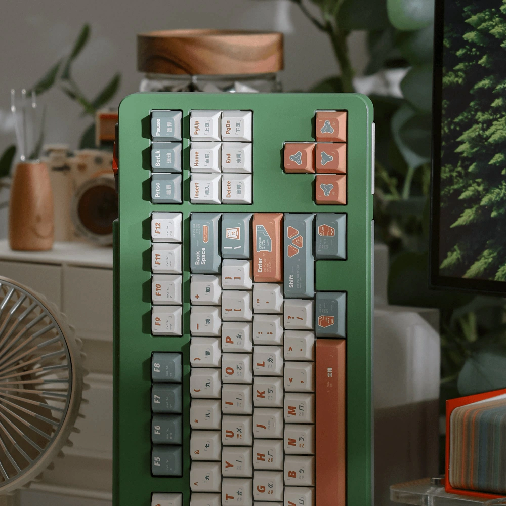 Green keyboard with white, gray-green, and salmon GUARDIAN keycaps, shown upright beside a monitor.