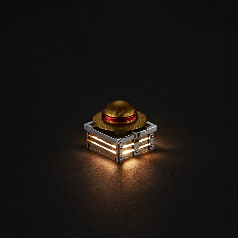 Rotating Straw Hat Aluminum Artisan Keycap Gold and red hat keycap glowing against a dark surface.