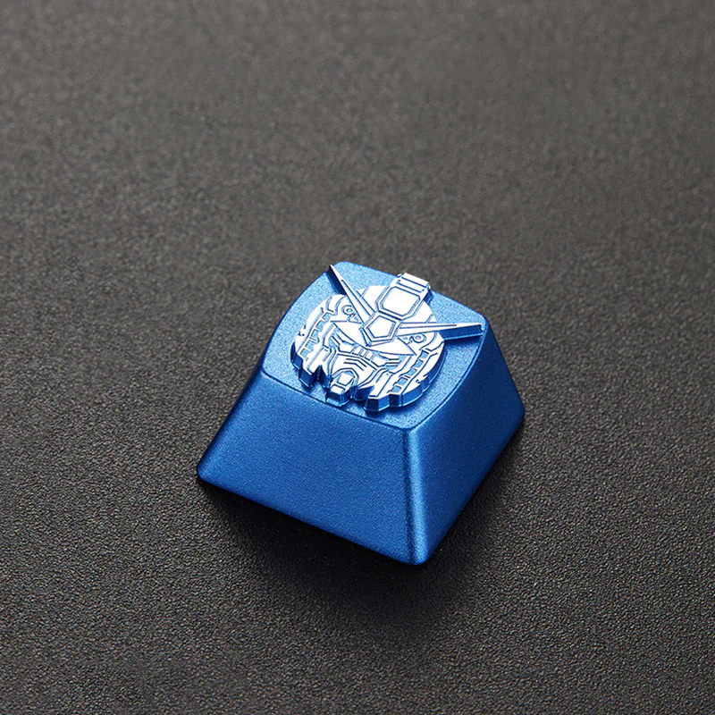 Blue metal mecha head keycap viewed at an angle on a dark textured surface.