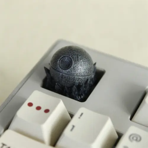 A dark gray spherical Death Star keycap sits in a light keyboard, viewed from above.