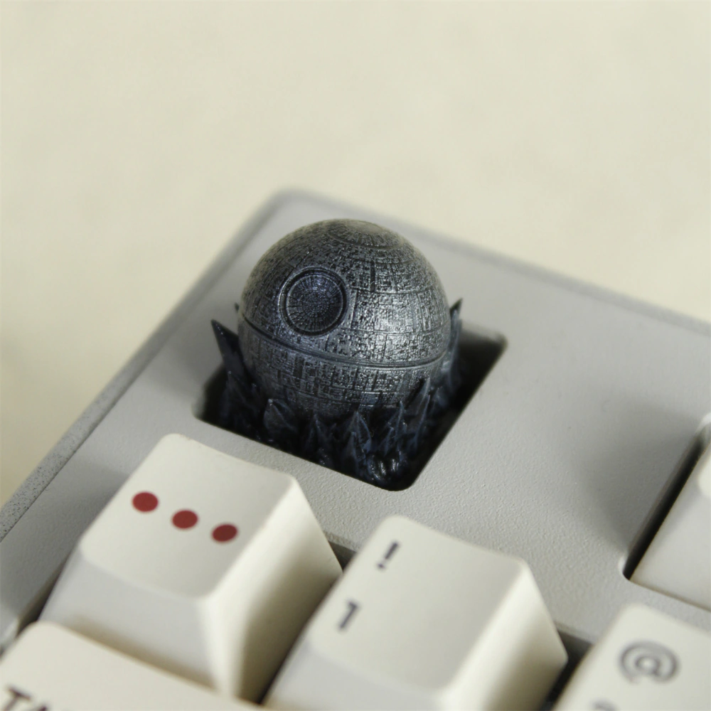 A dark gray spherical Death Star keycap sits in a light keyboard, viewed from above.