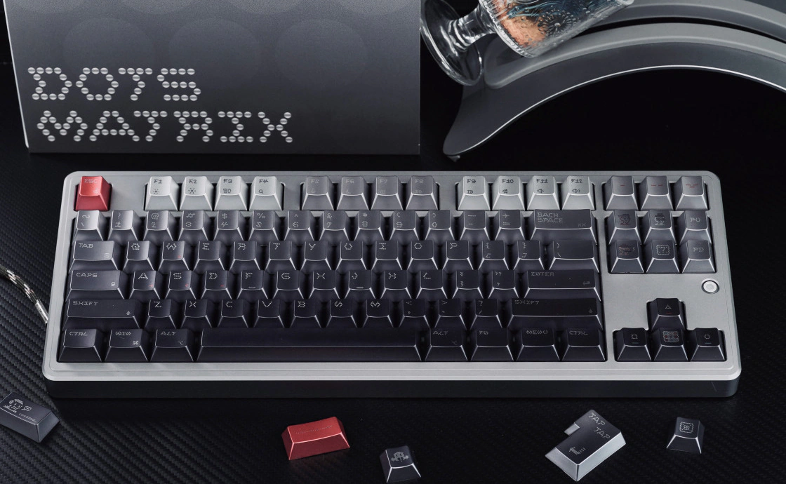Keyboard fitted with gray dot-matrix keycaps and red accents on a dark surface.