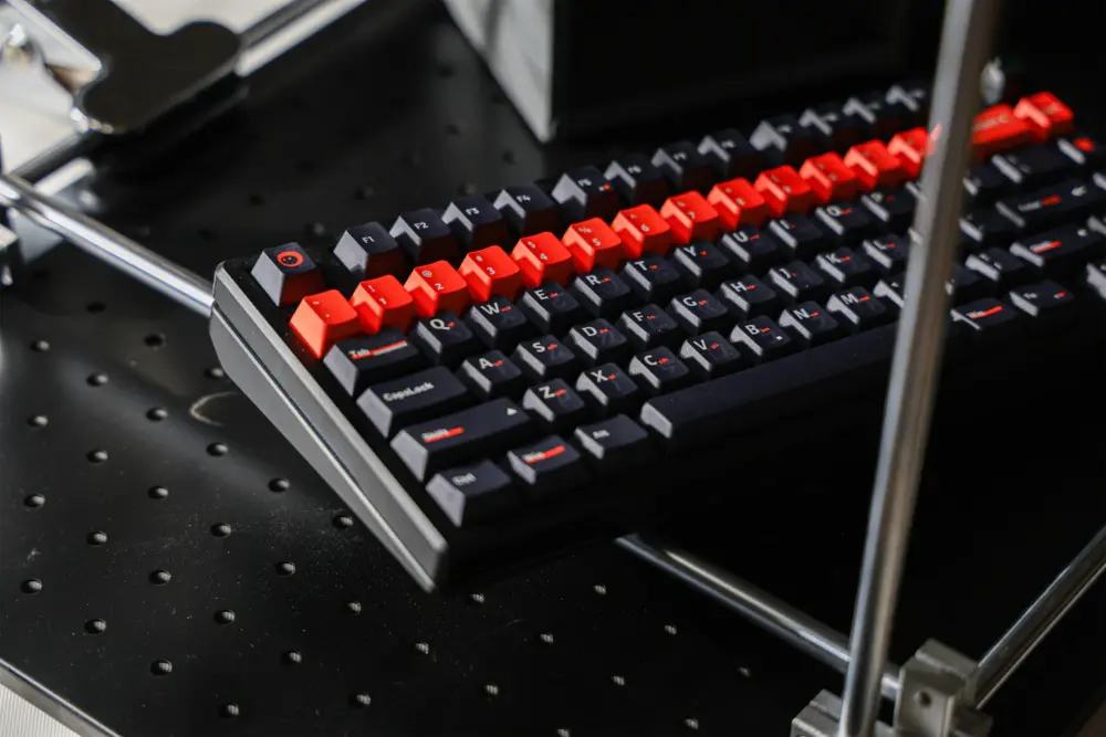 Black keyboard with dark and orange keycaps resting on a metal stand.