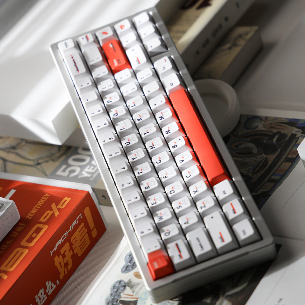 White keyboard with orange keys shown at a steep diagonal among books.