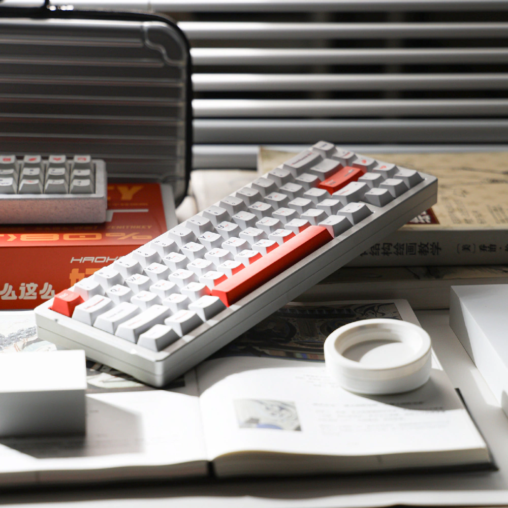 White keycaps with orange accents on a gray keyboard among books and desk items.