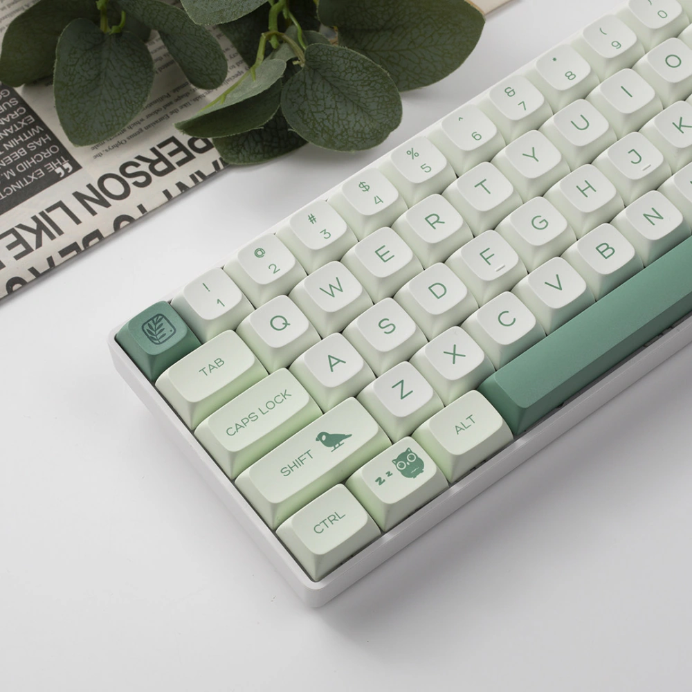 Green Botanical Keycaps Leaf Detail Close-up of green and white keycaps with visible leaf, bird, and owl illustrations.
