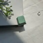 Green heart artisan keycap with heartbeat engraving shown at an angle on a book
