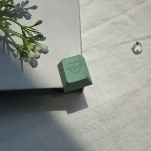Green heart artisan keycap with heartbeat engraving shown at an angle on a book