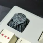 A gray Millennium Falcon spacecraft keycap sits in a light keyboard, viewed from above.