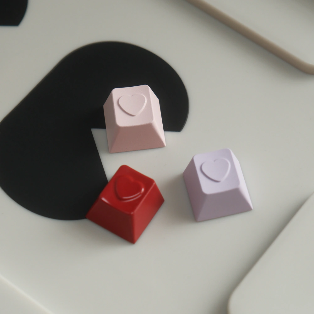 Three loose heart-shaped keycaps in red, lavender, and pale pink.