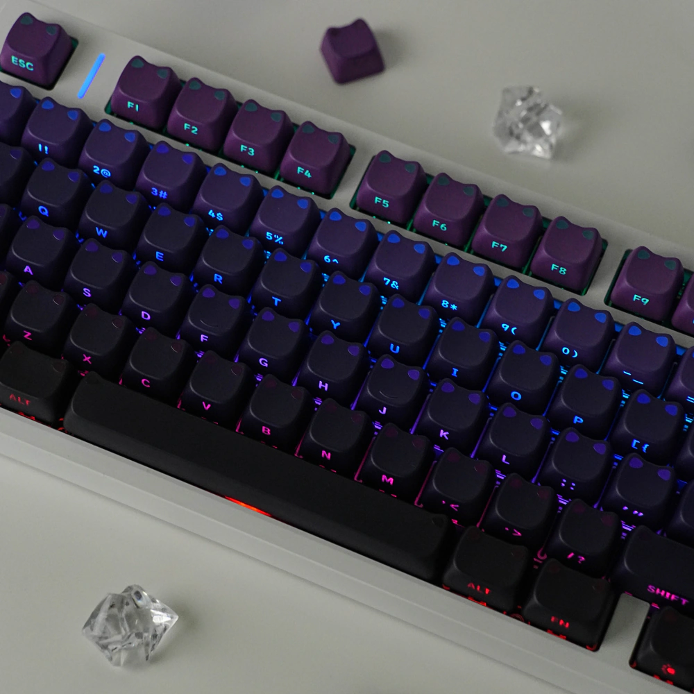 Close-up of purple and black cat-ear keycaps with illuminated legends and gaps