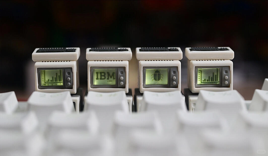 Row of four beige mini computer keycaps on white keys, with bar charts, IBM text, and an insect icon on their screens.
