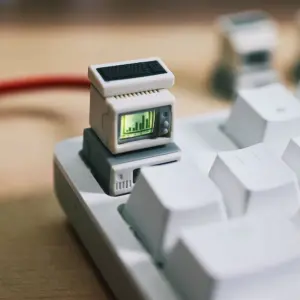 Close-up of a beige mini computer keycap with a green bar graph screen and black mini keyboard above white keys.