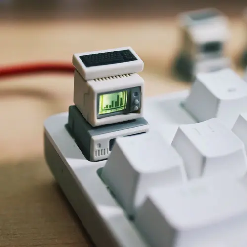Close-up of a beige mini computer keycap with a green bar graph screen and black mini keyboard above white keys.