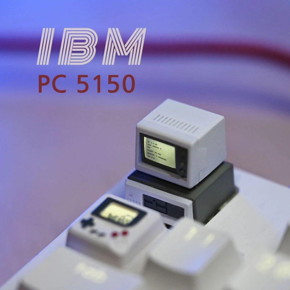 Miniature beige computer keycap on a white keyboard beneath large IBM PC 5150 text against a purple background.