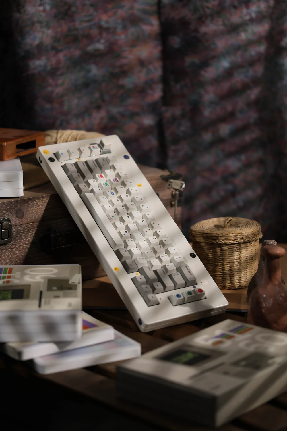 White and gray keycaps on a keyboard propped against wooden boxes, with printed cases in the foreground.