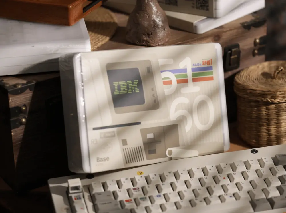 White and gray keyboard in front of a clear printed case showing IBM 5160 Base artwork.