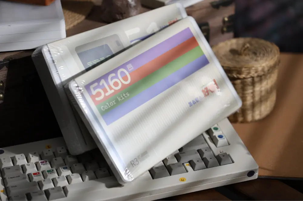 Printed Color Kits box laid across a white and gray keyboard on a wooden desk.