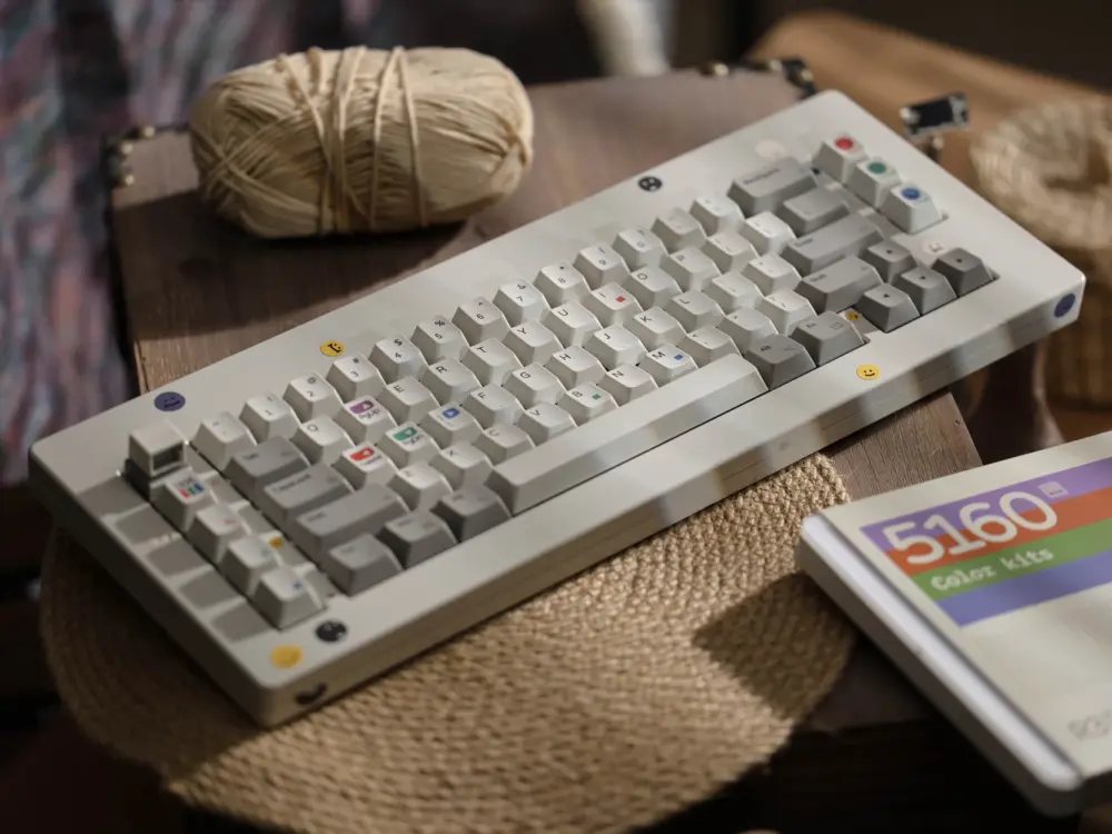 White and gray keycaps on a keyboard resting on a round woven mat beside a printed box.