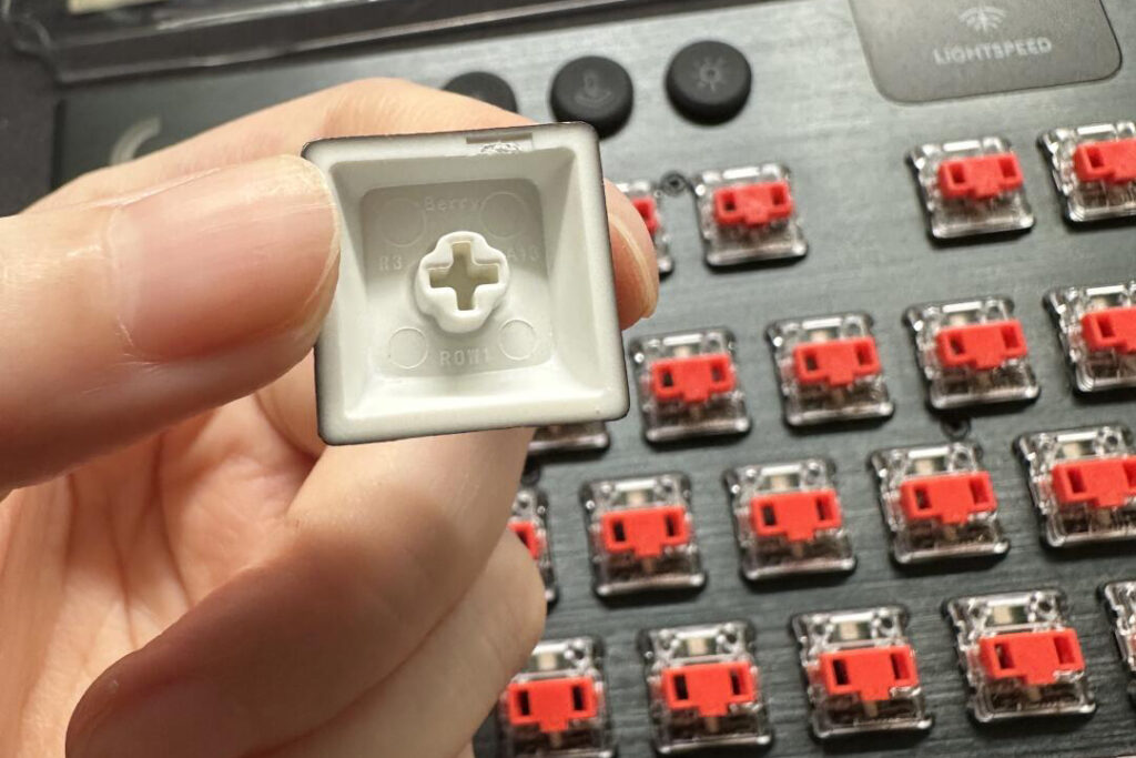 Hand holding the underside of a cross-mount keycap above exposed red switch stems