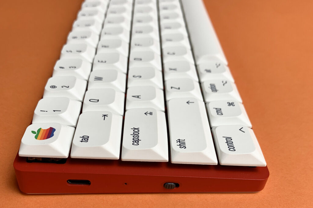 Low-profile white keyboard photographed from the front on an orange surface