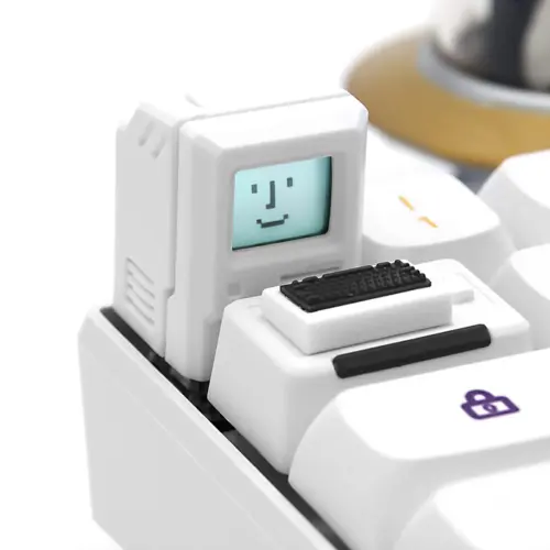 White computer-shaped keycap with a pixel face on its screen, installed beside its mini keyboard piece.