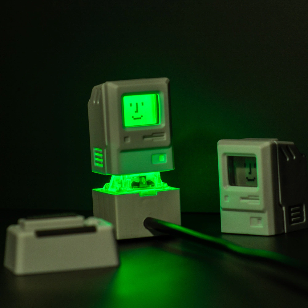 Two miniature computer caps on a clear base glowing green against a dark background.