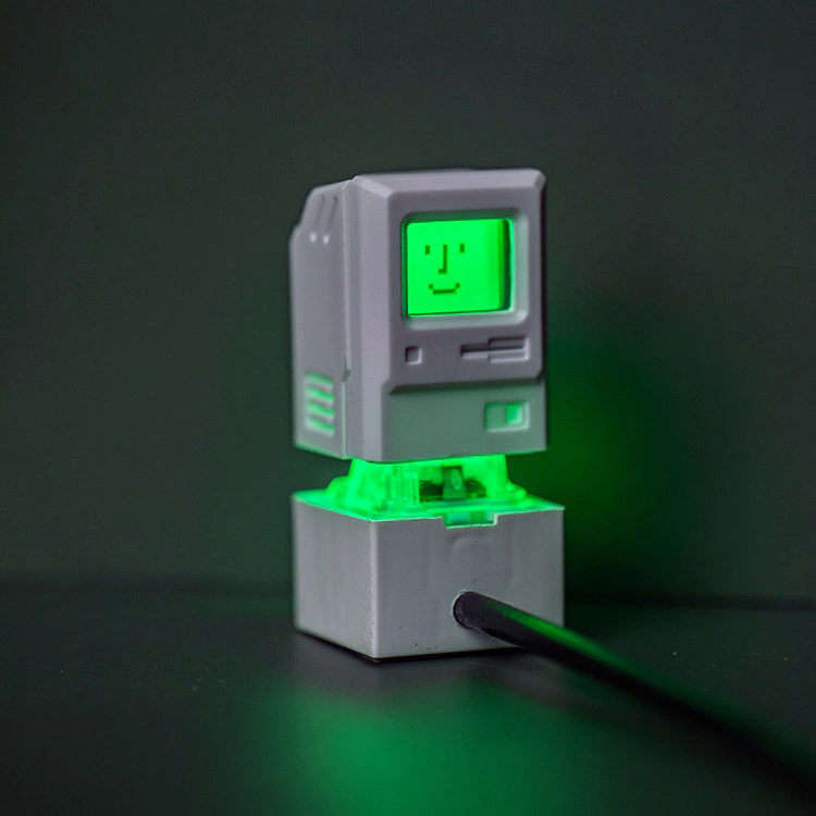 White miniature computer cap above a clear base glowing green, with a cable visible beside it.
