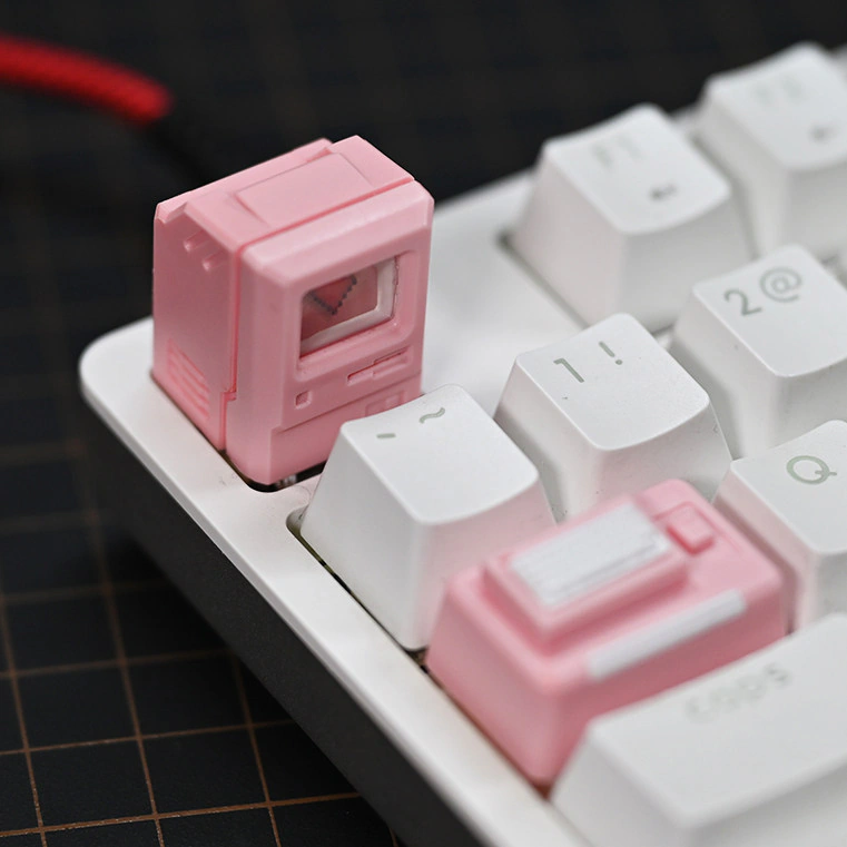 Pink computer-shaped keycap with a pixel heart on its screen and a small keyboard piece among white keys.