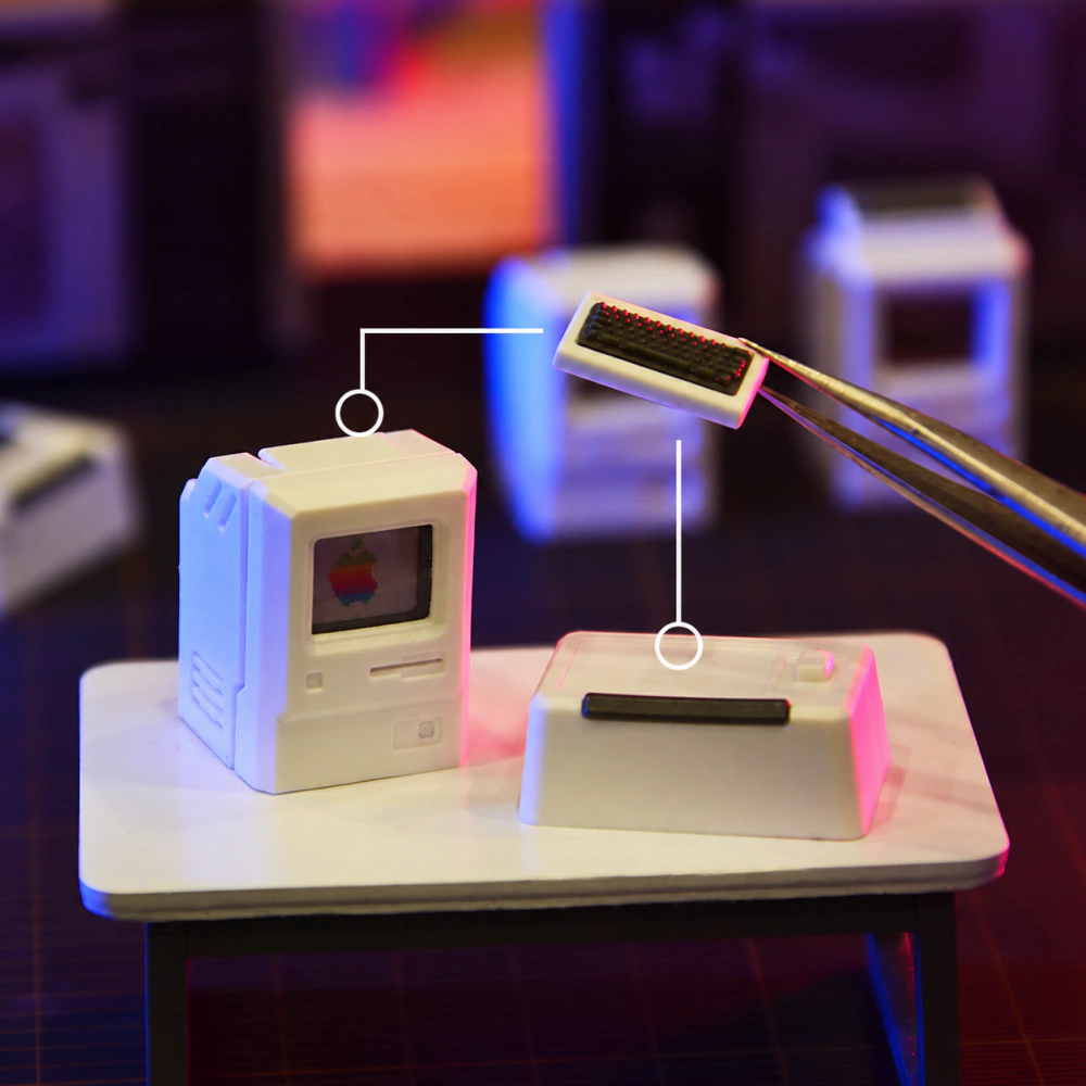 Miniature computer keycaps on a tabletop, with tweezers holding the small keyboard piece beside a placement diagram.
