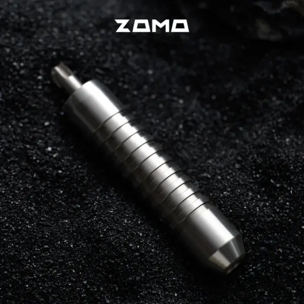 A silver grooved ZOMO adjuster lies diagonally on a black textured surface.