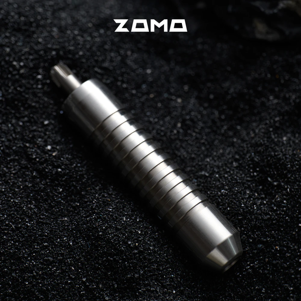 A silver grooved ZOMO adjuster lies diagonally on a black textured surface.